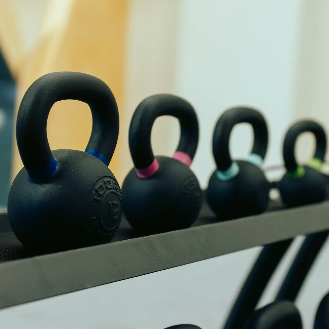 Vier schwarze Kettlebells in verschiedenen Größen mit farbigen Akzenten auf einem Regal.