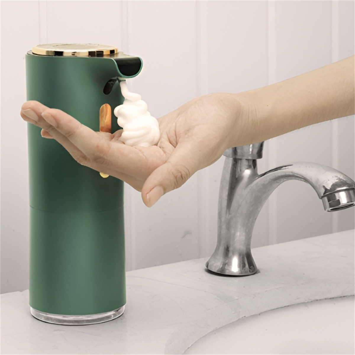 Grüner automatischer Seifenspender, der Schaum in eine Hand abgibt. Weißes Waschbecken und Wasserhahn im Hintergrund.