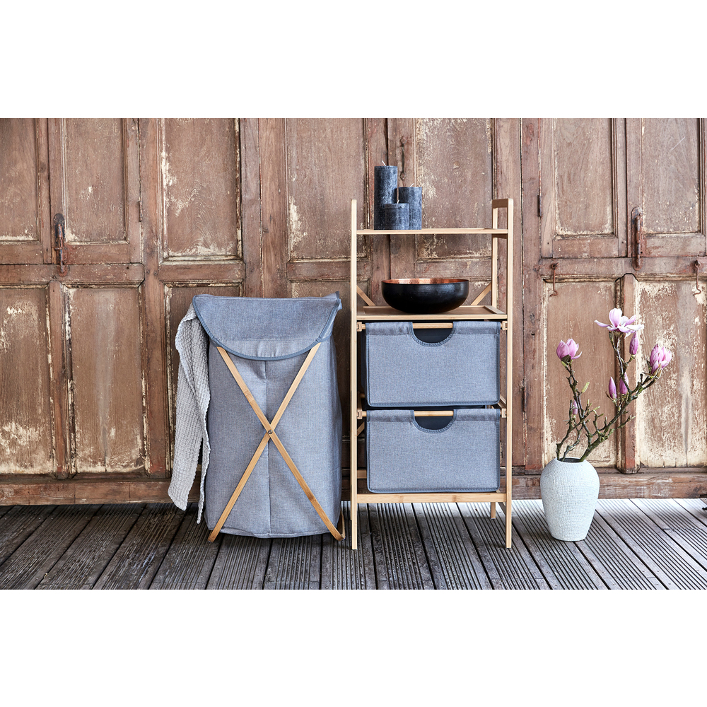Ein grauer Wäschekorb mit Holzrahmen. Daneben ein Holzregal mit Aufbewahrungsboxen und einer Vase mit Blumen.