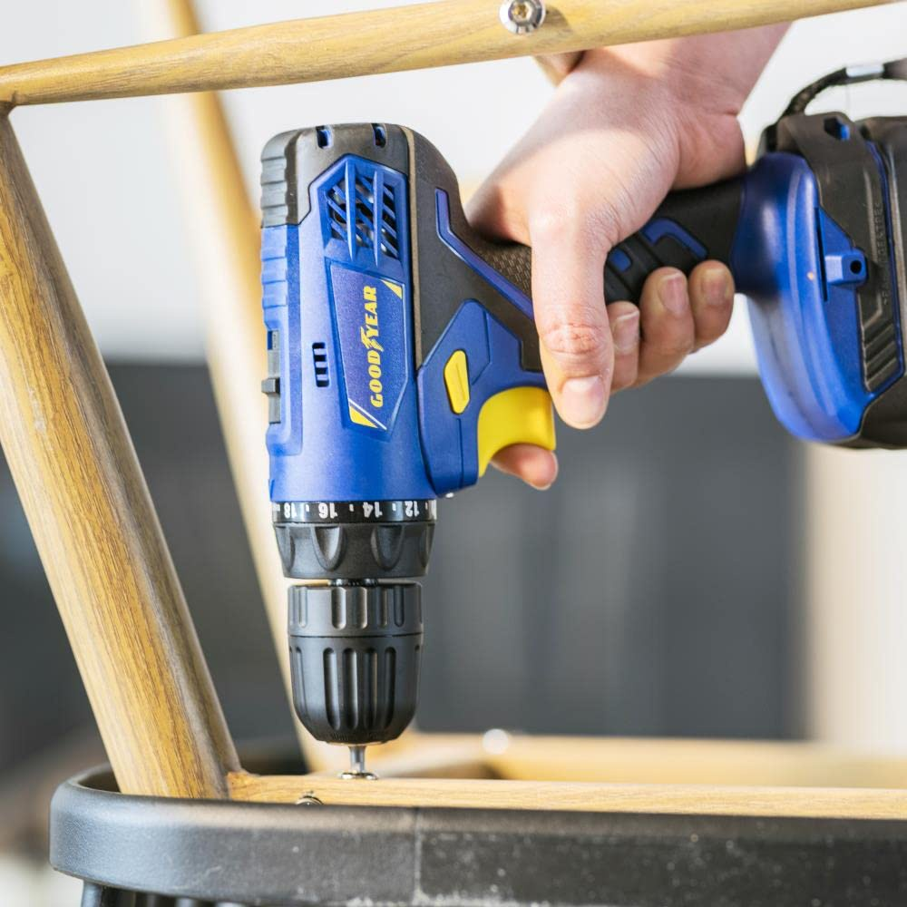 Una mano usa un taladro Goodyear azul y negro para atornillar un marco de silla de madera.