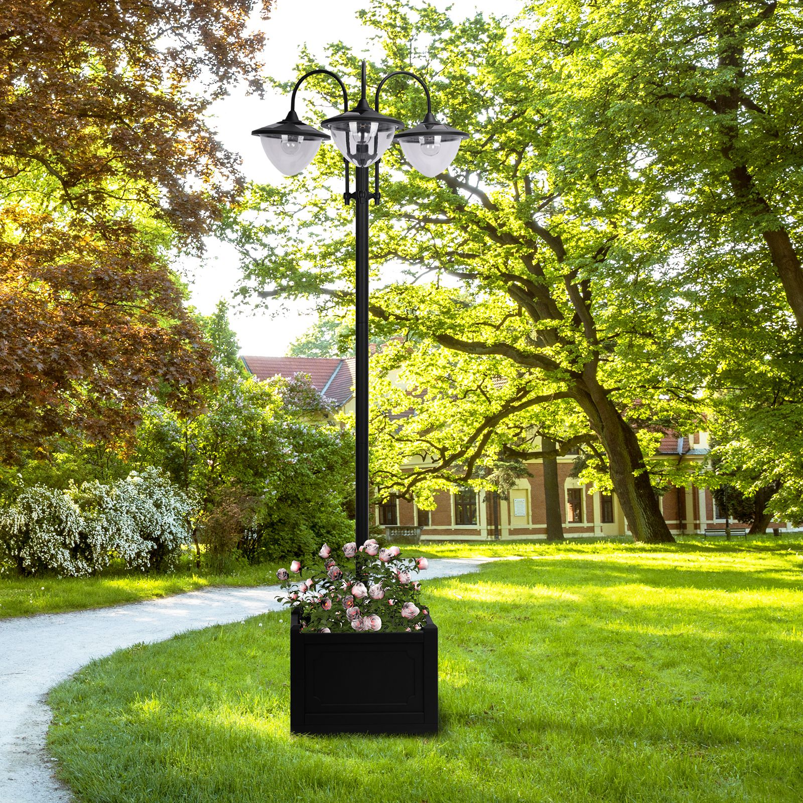 Parkszene mit Laternenpfahl, Blumenkasten und Gehweg. Bäume und grünes Gras im Hintergrund.
