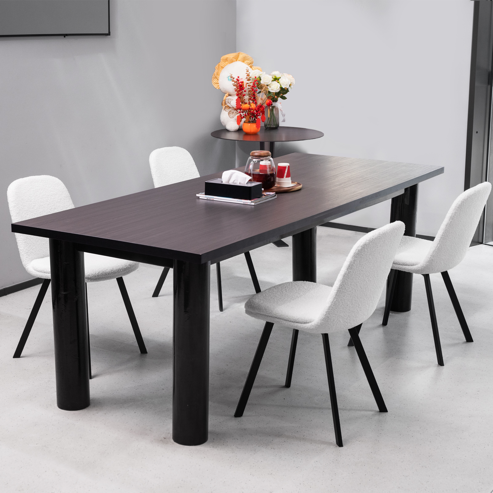 Dunkler Holztisch mit vier weißen Stühlen. Kleiner Tisch mit Blumen und Teddybär im Hintergrund.
