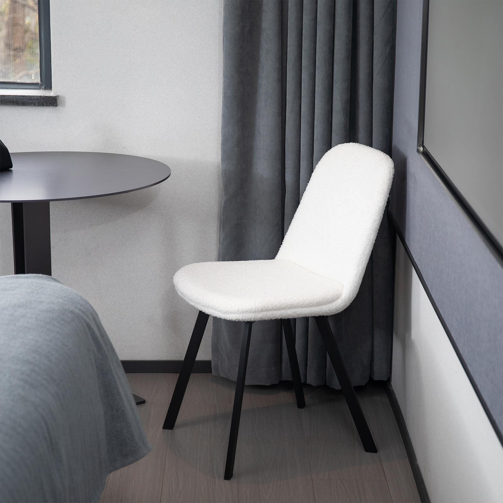 Ein weißer Stuhl mit schwarzen Beinen in einem Raum. Ein Tisch und ein Fenster sind im Hintergrund.