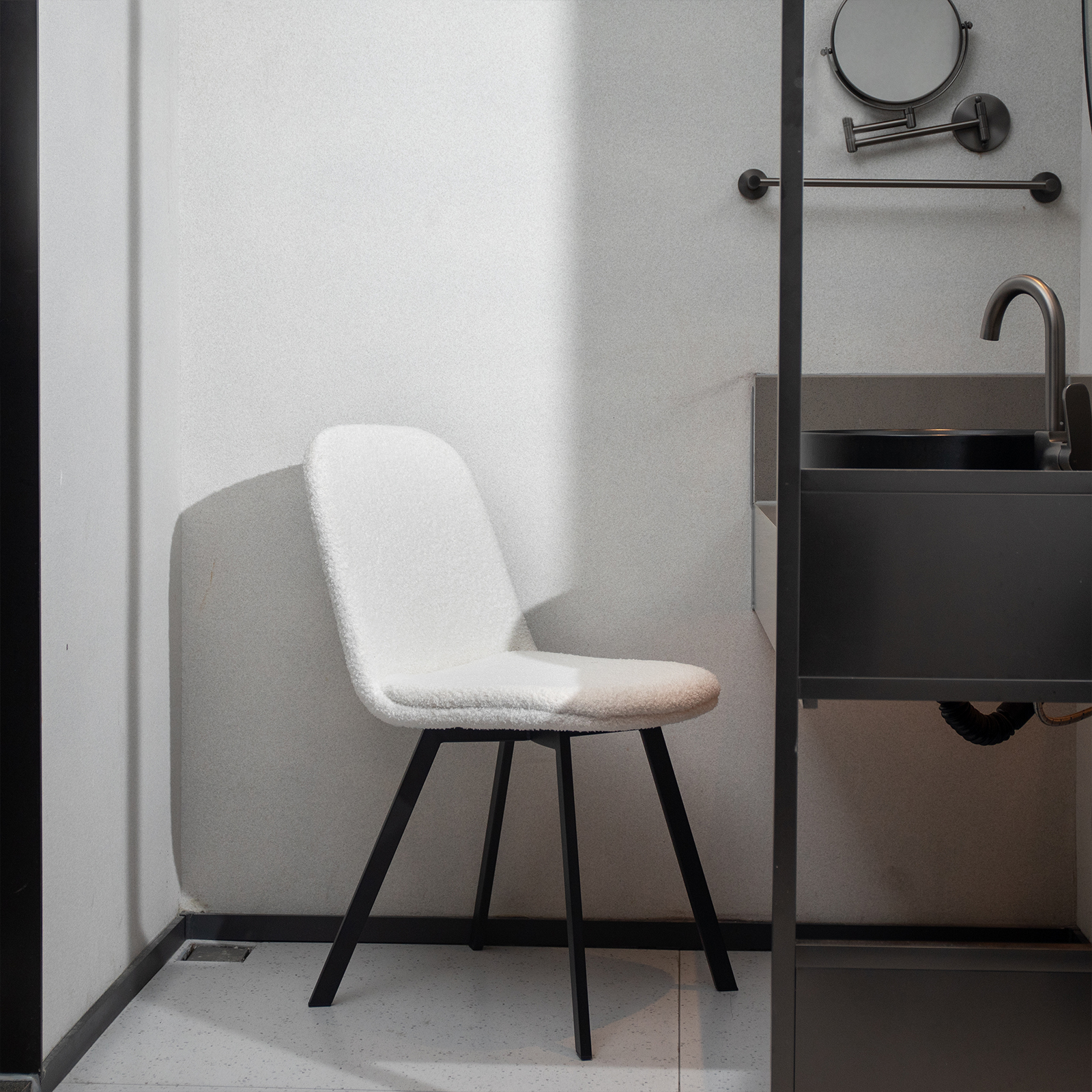 Badezimmer: weißer Stuhl, schwarzes Waschbecken, Spiegel und Handtuchhalter.