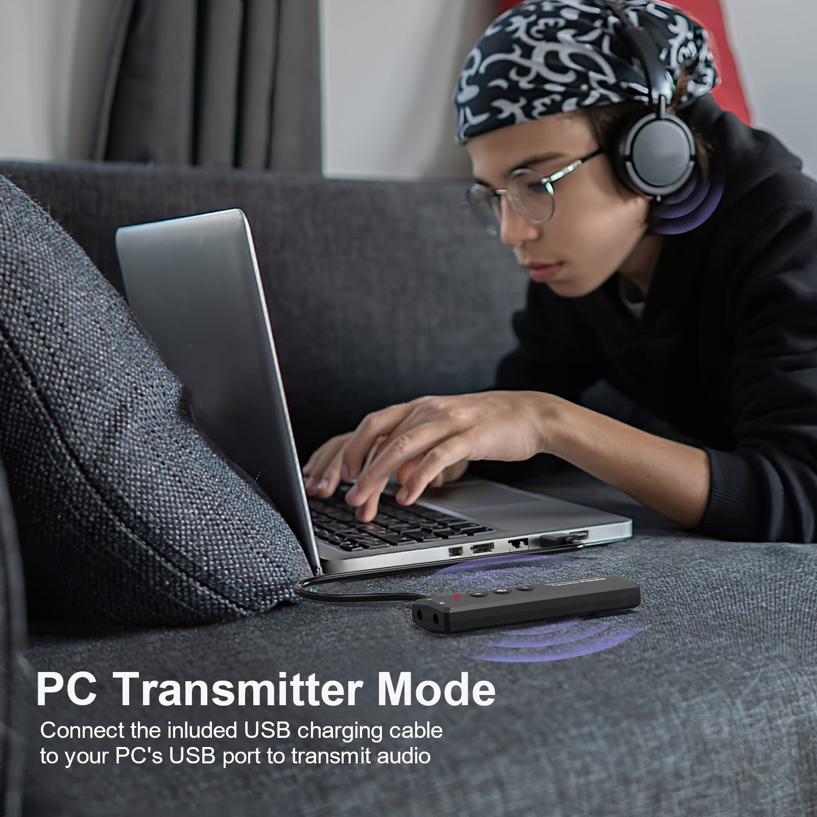 Person mit Kopfhörern und Laptop, kleines schwarzes Gerät auf dem Sofa, in der Nähe eines Ladekabels.