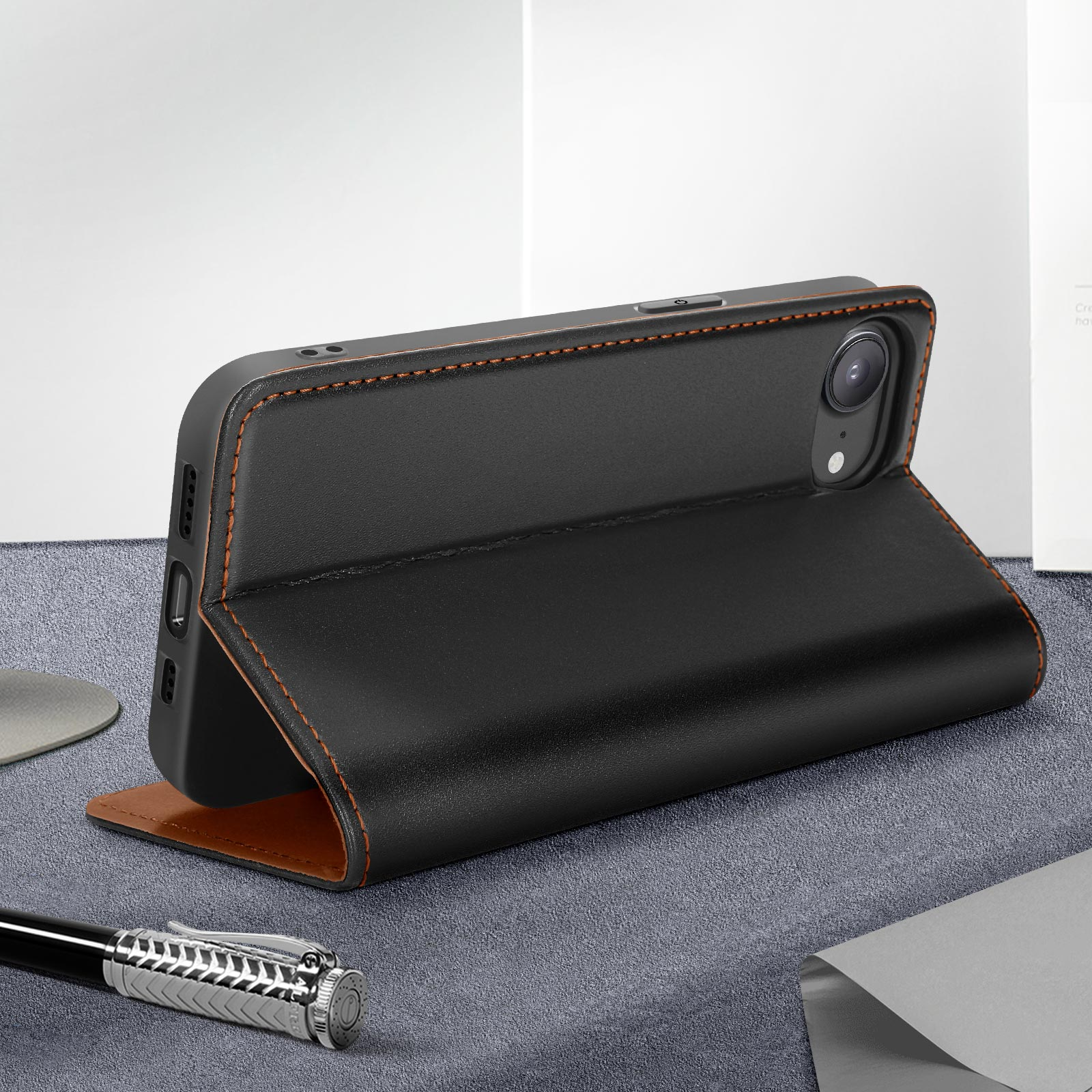 Funda de teléfono negra abierta con un teléfono dentro. Descansa sobre una superficie gris. Costuras marrones.