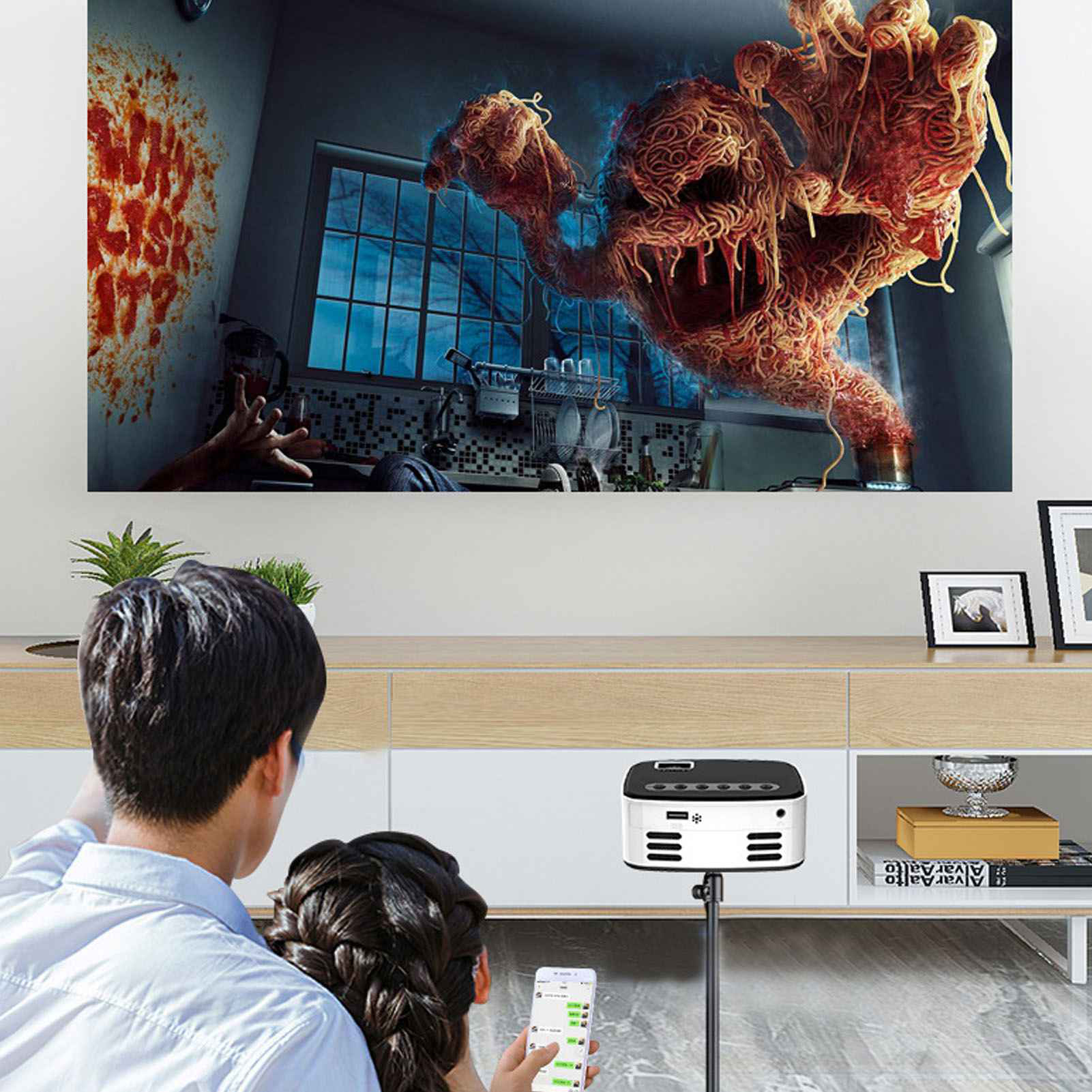 Menschen, die einen Projektorbildschirm betrachten, der ein Monster aus Spaghetti in einer Küche zeigt.