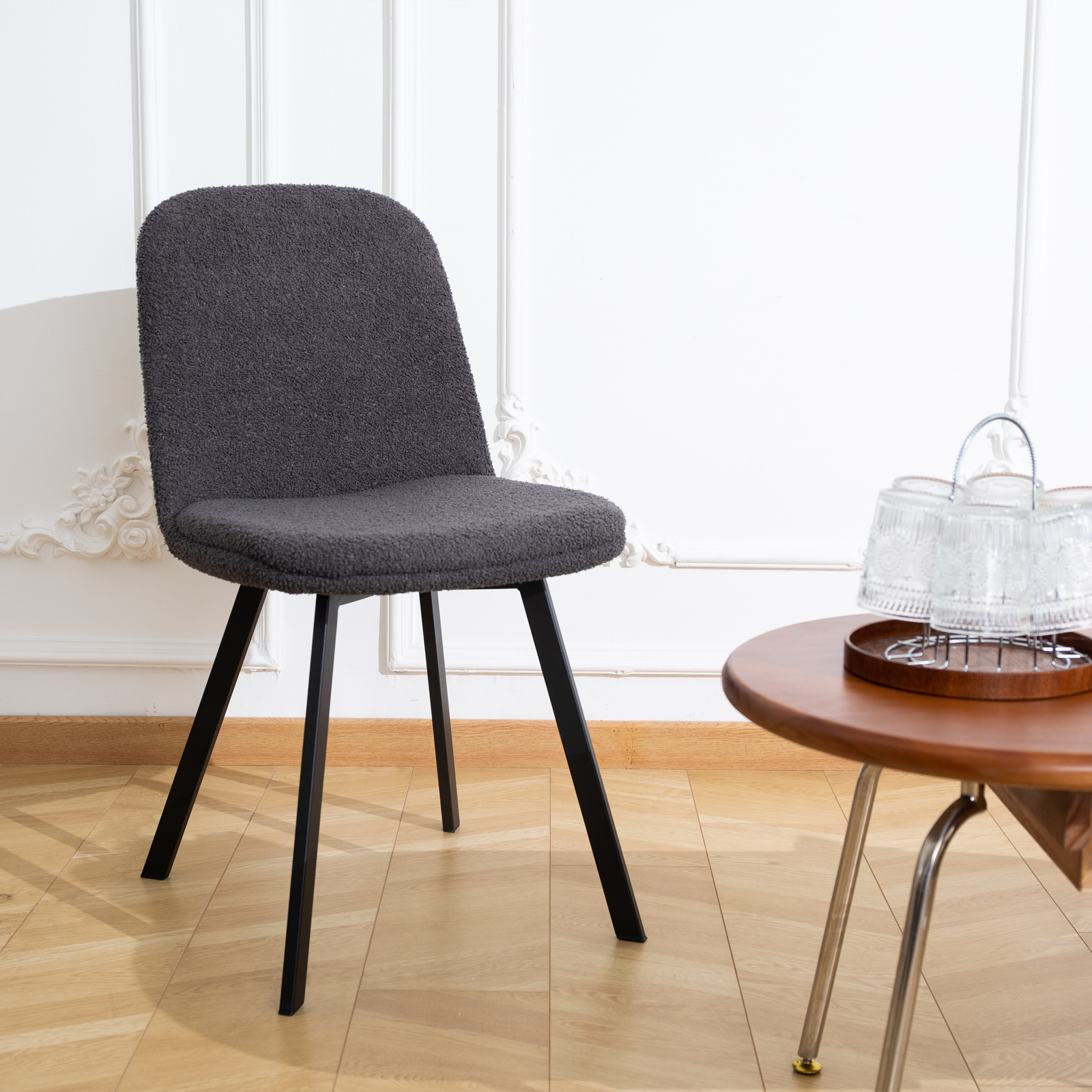 Ein grau gepolsterter Stuhl mit schwarzen Beinen und ein runder Beistelltisch aus Holz.
