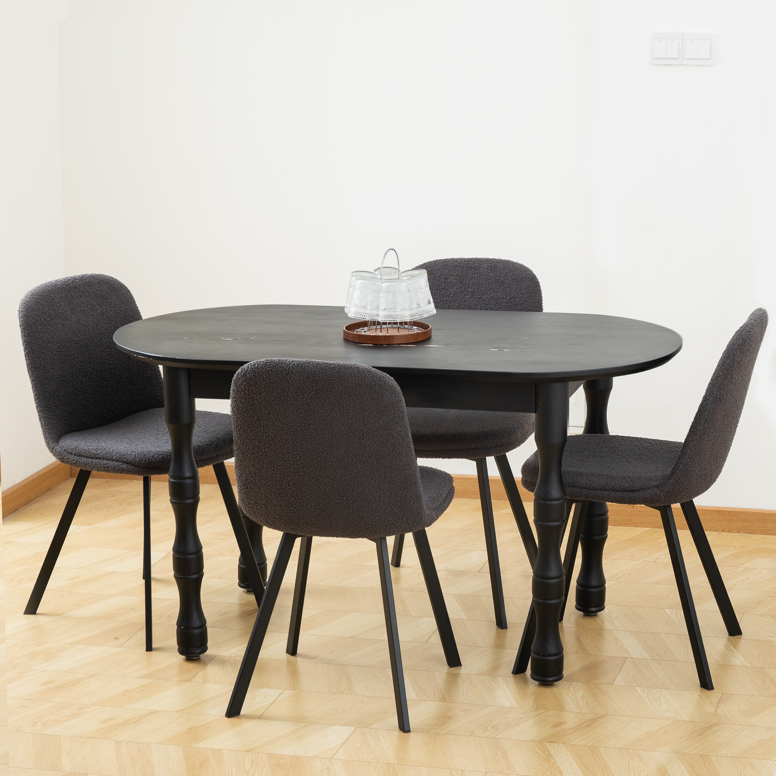 Esszimmer-Set mit einem schwarzen, ovalen Tisch und vier grauen Stühlen. Heller Holzboden.