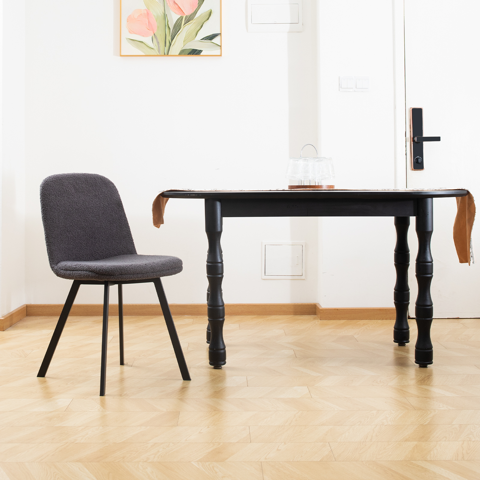 Schwarzer Tisch und grauer Stuhl in einem Raum mit Holzböden, Gemälde und Tür.