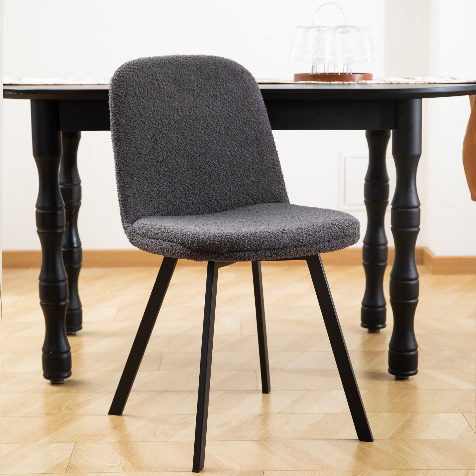 Ein grauer, flauschig gepolsterter Stuhl mit schwarzen Beinen vor einem schwarzen Tisch.