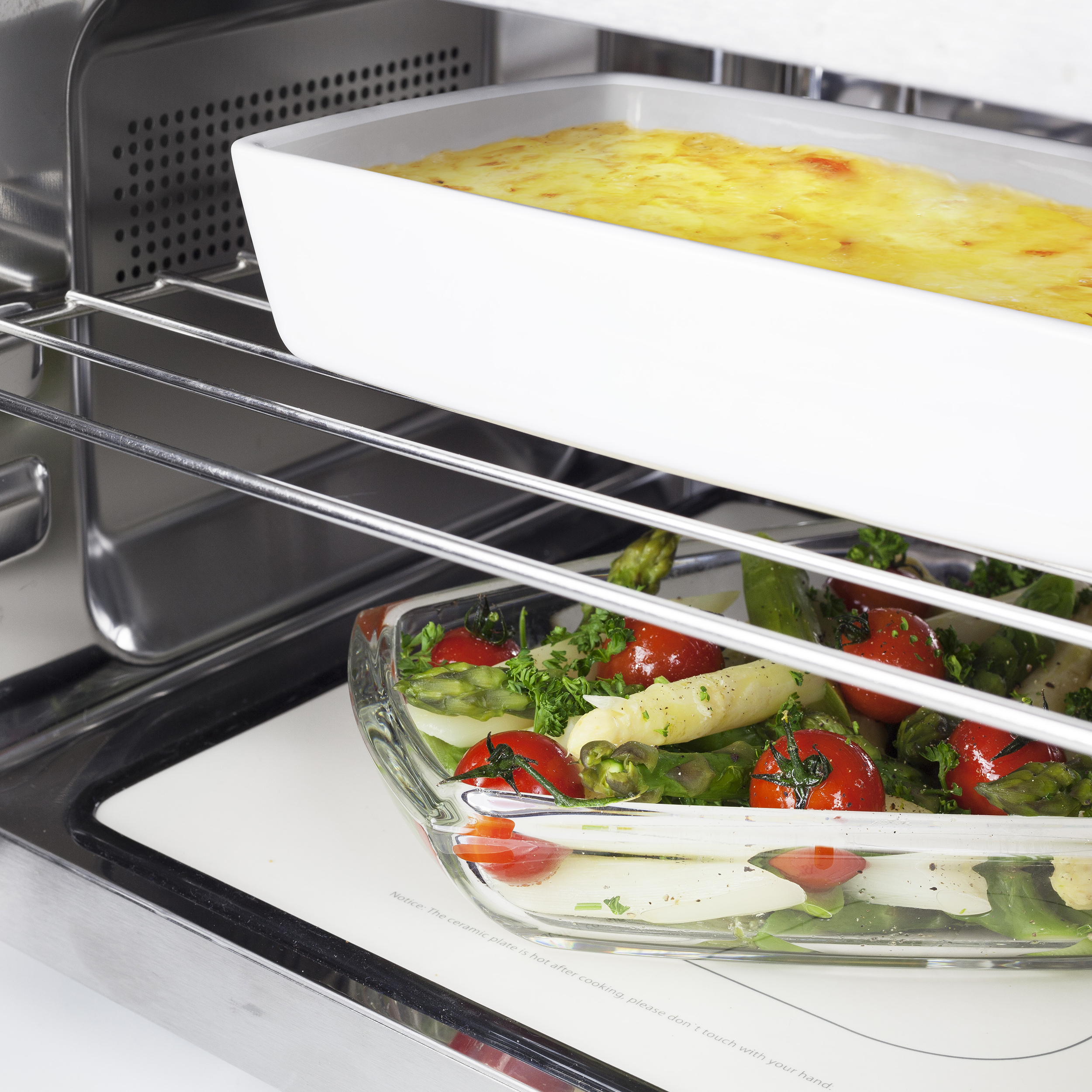 Interno di un forno con due piatti di vetro. Uno ha lasagne, l'altro verdure.