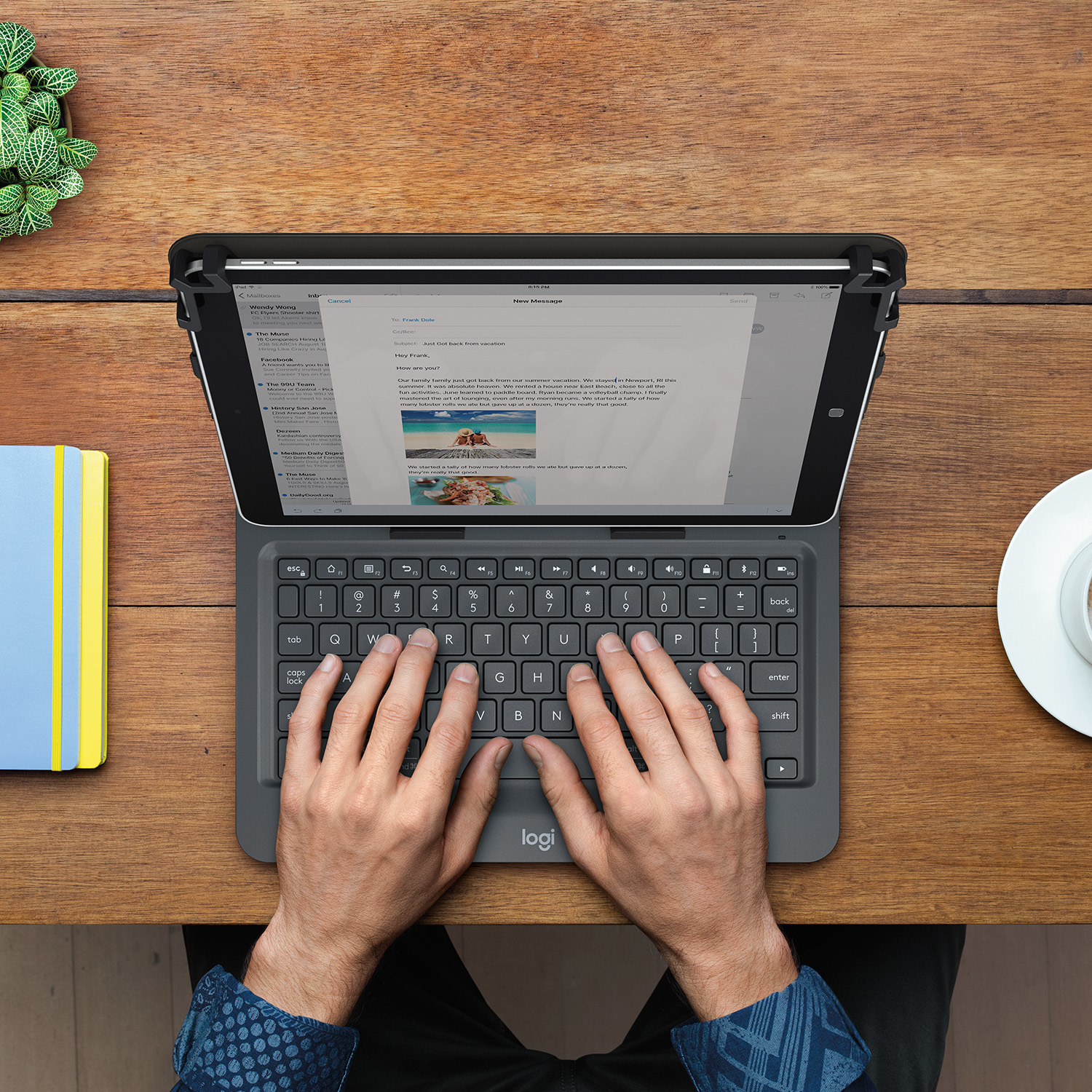 Mani che digitano su una tastiera per tablet, con un taccuino blu e giallo e una tazza di caffè sul tavolo.