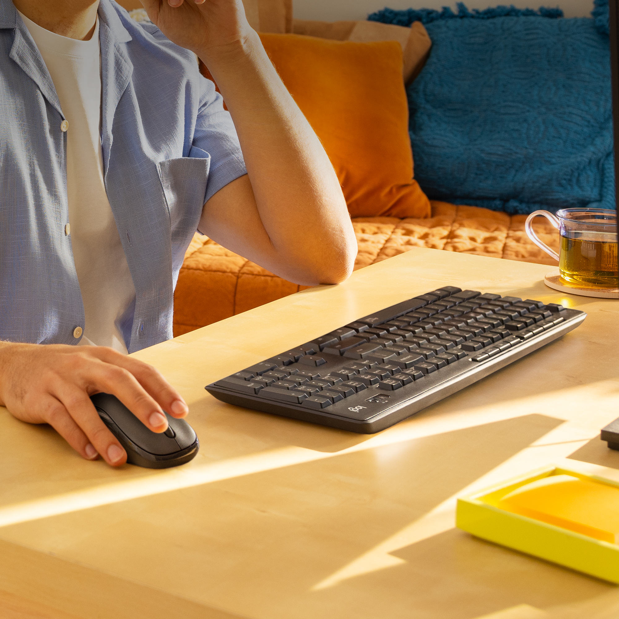 Mężczyzna używający klawiatury i myszy na drewnianym biurku. Są poduszki i herbata.