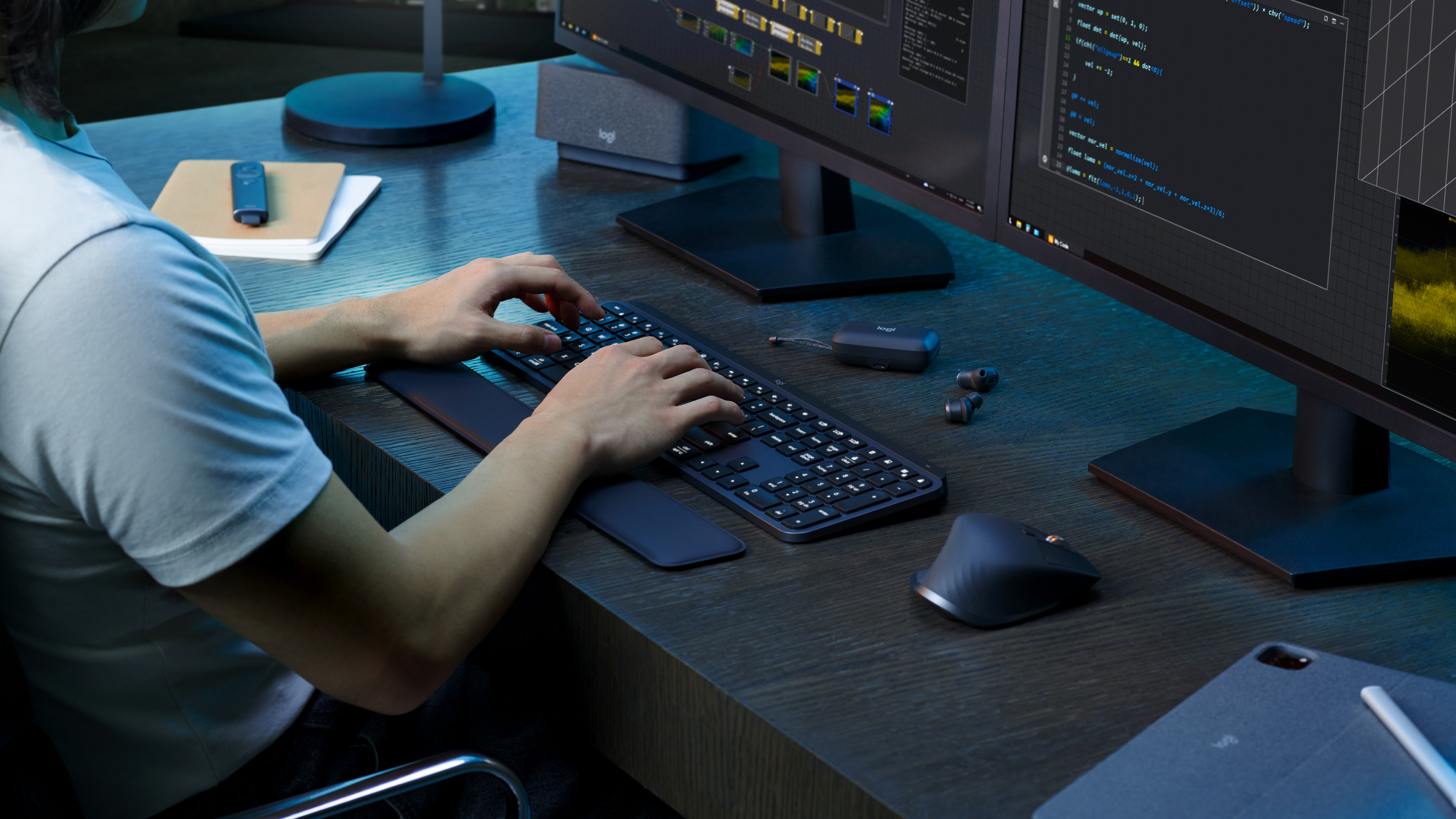 Osoba przy biurku pisząca na klawiaturze. Widoczne są dwa monitory, mysz i inne akcesoria komputerowe.