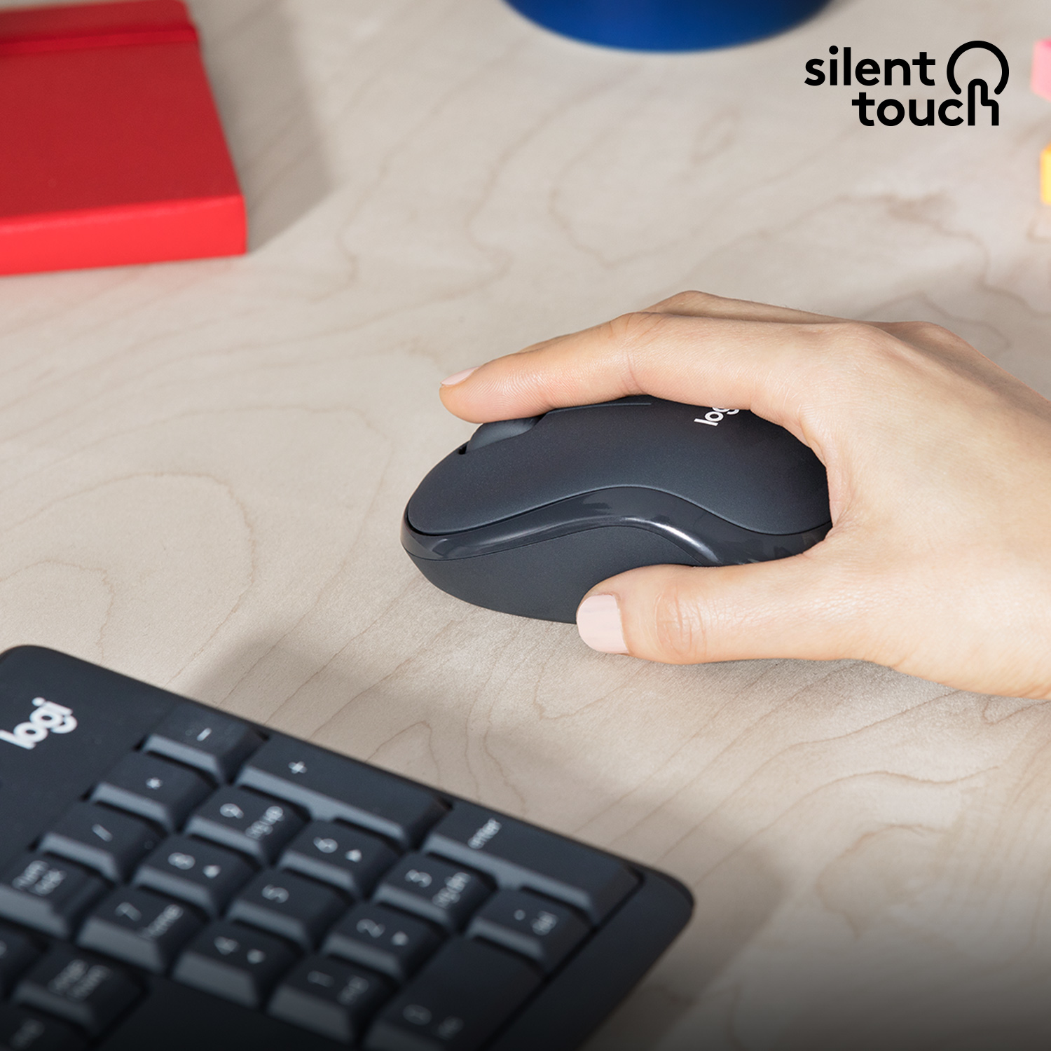 Die Hand einer Person auf einer dunkelgrauen drahtlosen Maus. Eine schwarze Tastatur befindet sich im Hintergrund, auf einer hellen Holzoberfläche.