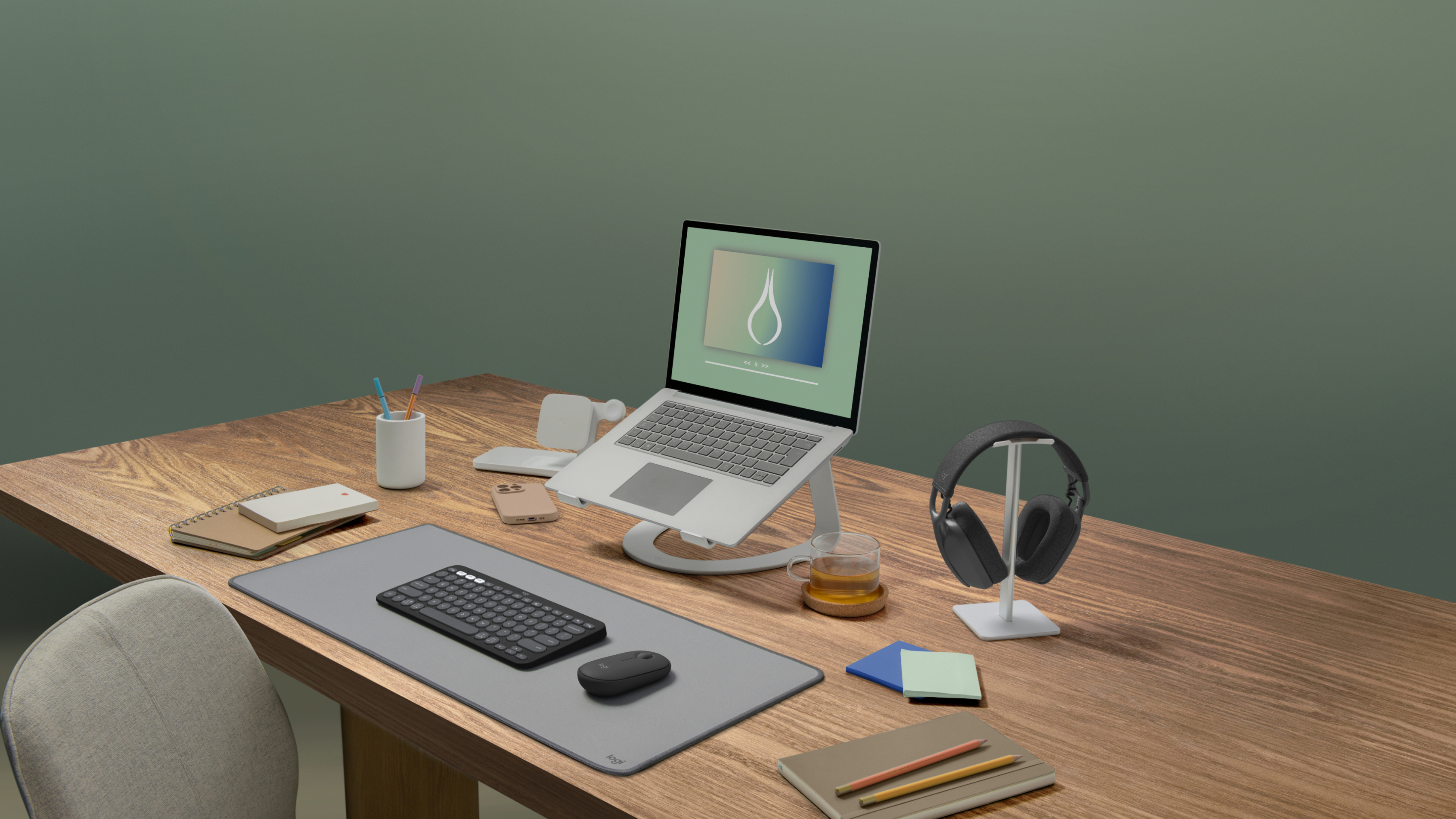 Drewniane biurko z laptopem, myszą, klawiaturą i słuchawkami. Tło jest zielone.