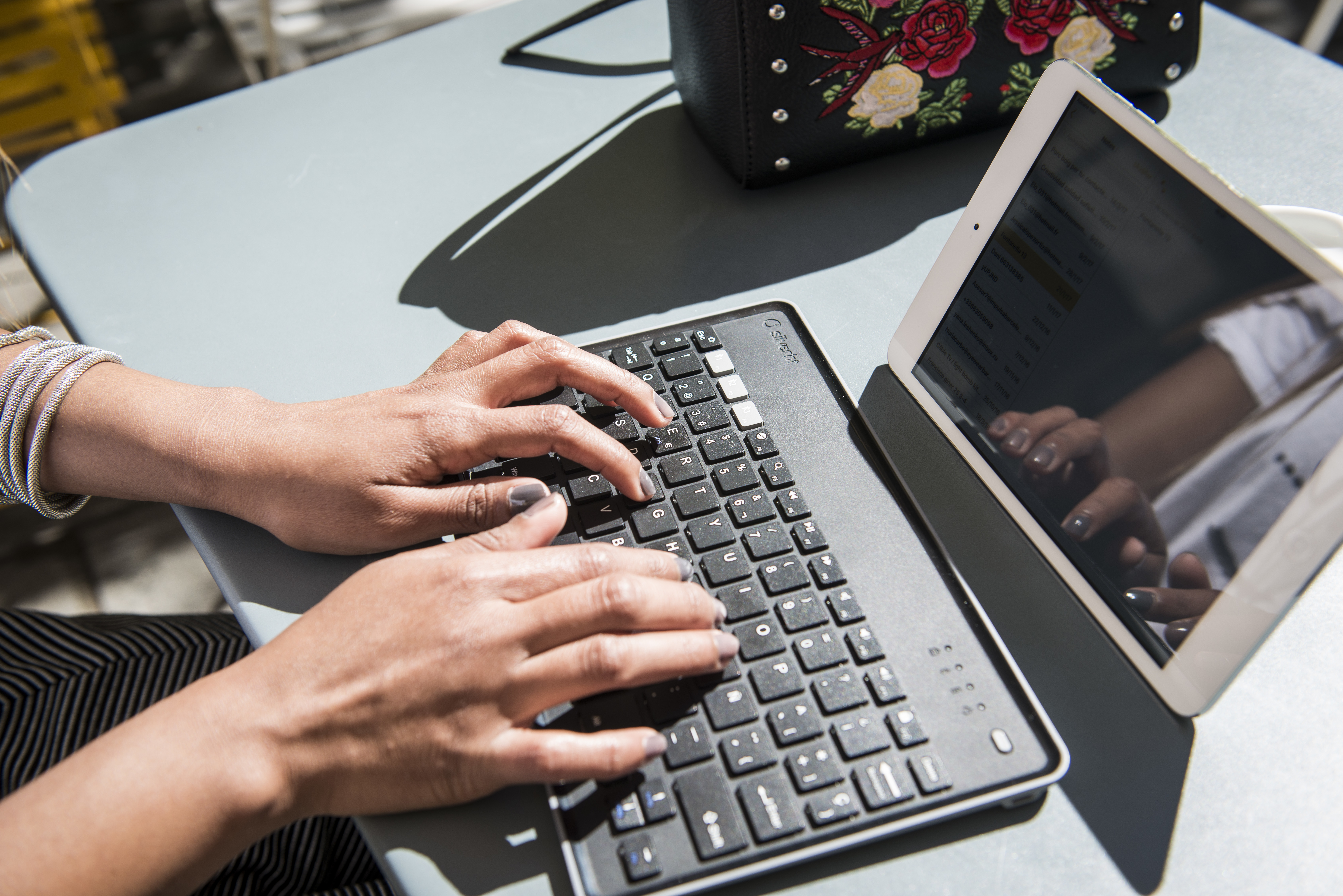 Dłonie piszące na czarnej klawiaturze z tabletem obok, na stole.