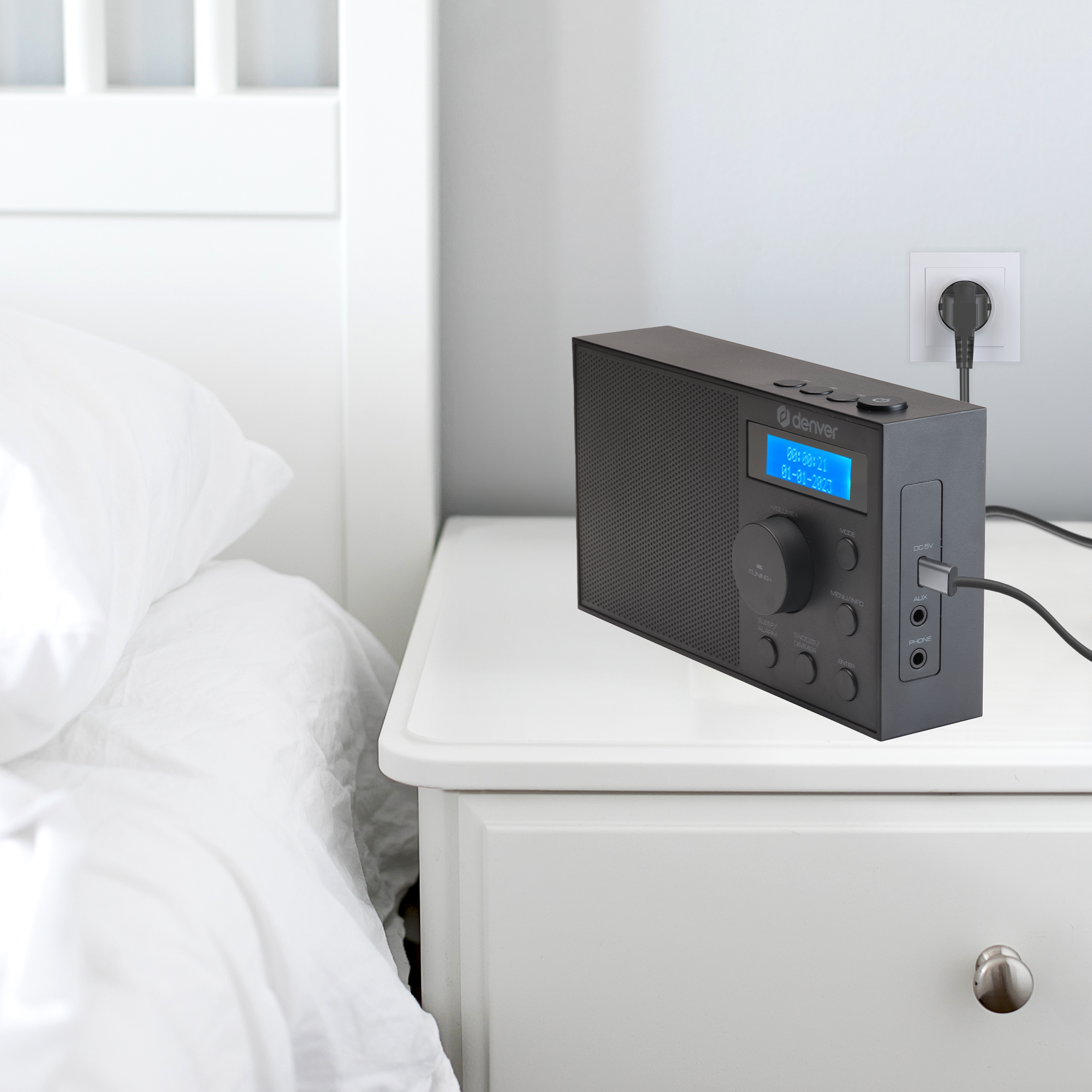 Czarny radio na białej szafce nocnej. W tle łóżko.