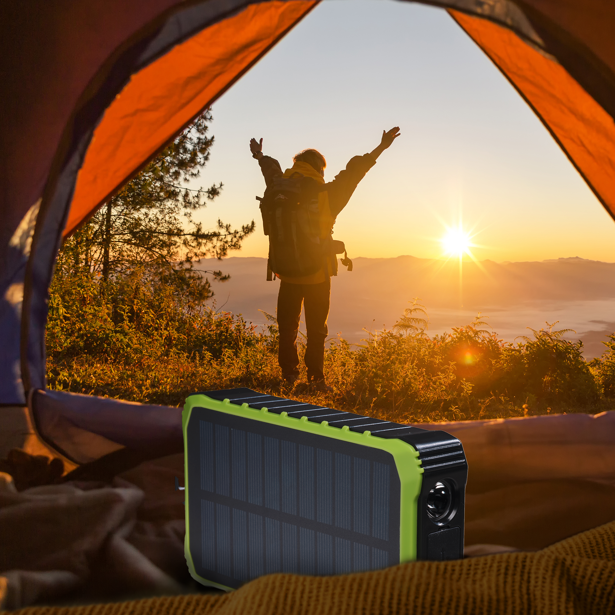 Personne debout, bras levés devant une tente, face au coucher du soleil. Chargeur solaire au premier plan.