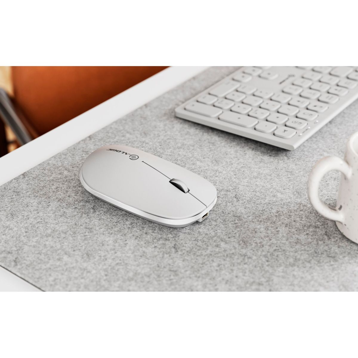 Un mouse bianco su una superficie grigia con una tastiera bianca e una tazza sullo sfondo.