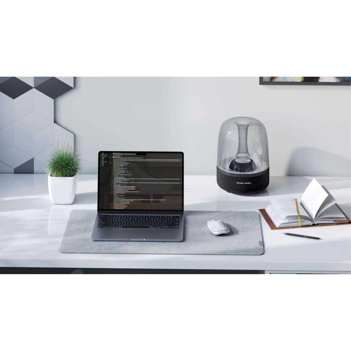Una scrivania con laptop, altoparlante, mouse, libro e pianta. Il laptop è aperto.