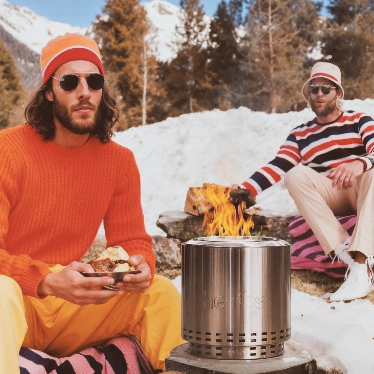 Zwei Männer am Feuer. Einer hält Essen, der andere am Metall-Feuerplatz in Schneegebiet.