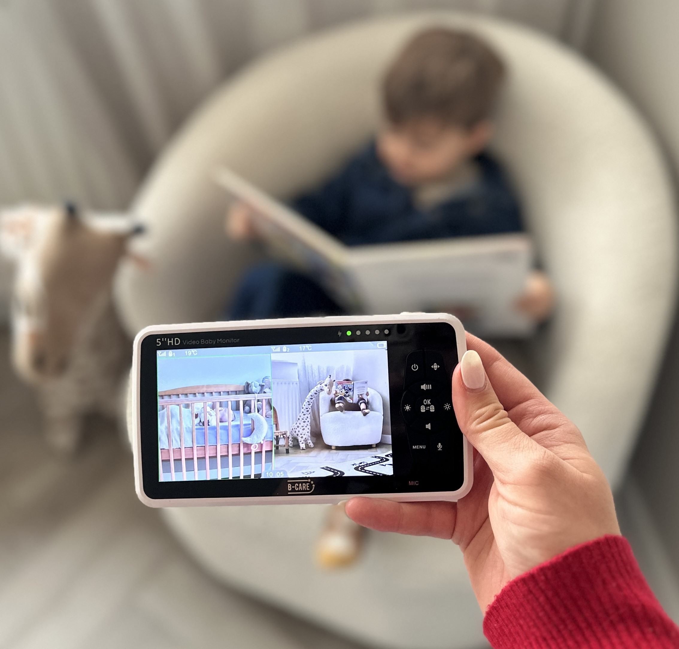 Babyphone-Bildschirm mit Kinderbett und Kind beim Lesen, gehalten von Hand.