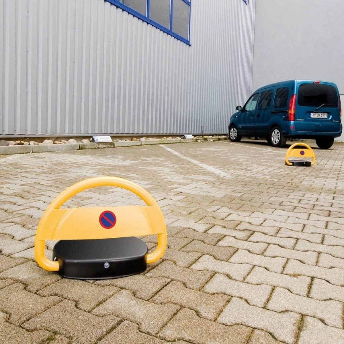 Gelbe Parkschranke vor einem Gebäude und einem Auto. Gepflasterter Parkplatz.