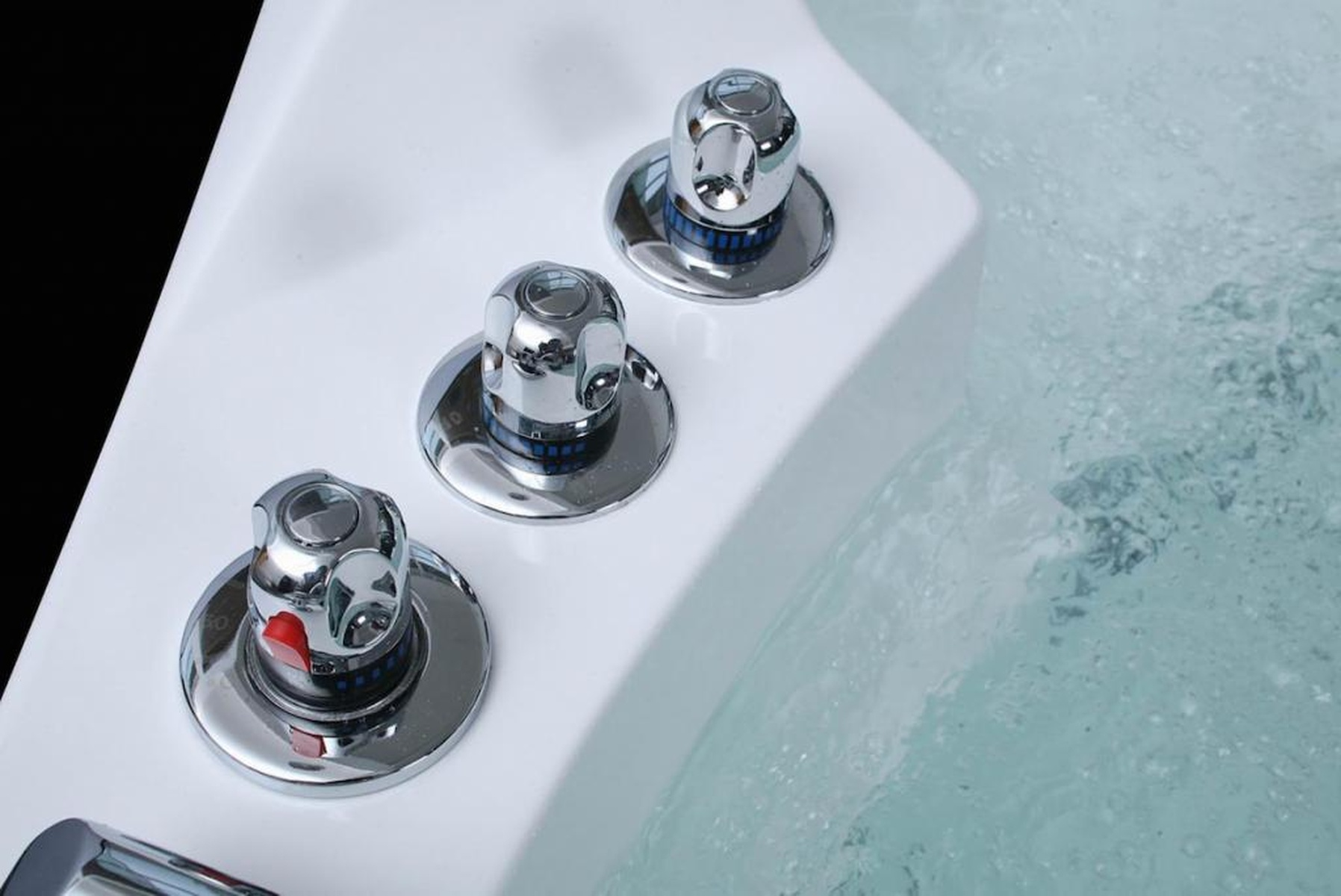 Nahaufnahme eines weißen Spa-Wannenbeckens mit drei Chrom-Steuerknöpfen und sprudelndem Wasser.