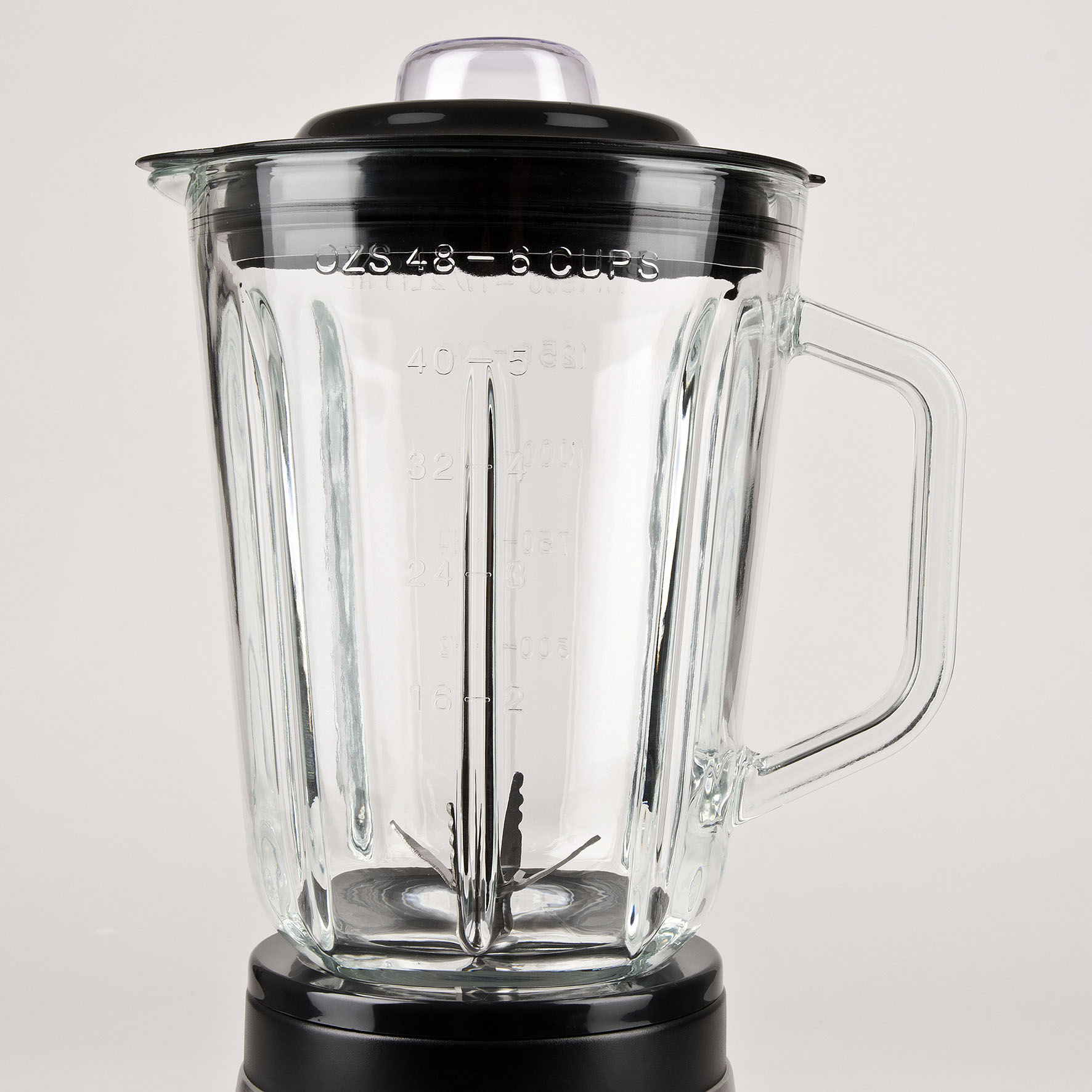 Bicchiere frullatore in vetro con coperchio e manico neri, lame in acciaio inox, sfondo bianco.