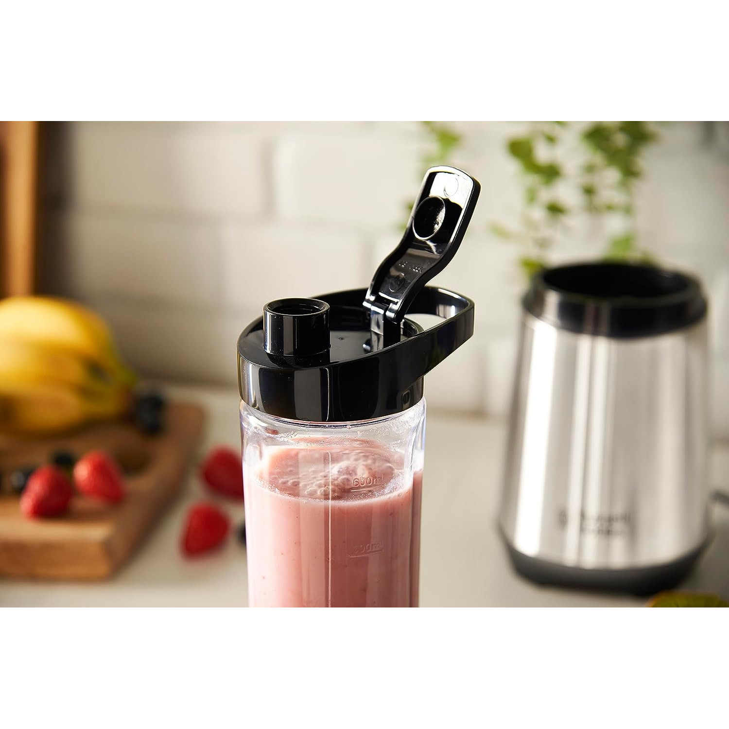 Ein Mixer mit einem rosa Getränk und einem schwarzen Deckel, mit einem zweiten Mixer im Hintergrund.