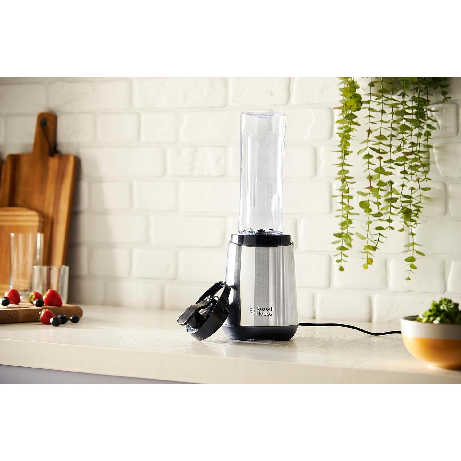 Ein Mixer steht auf einer Theke mit einem durchsichtigen Behälter, Beeren und Grün.