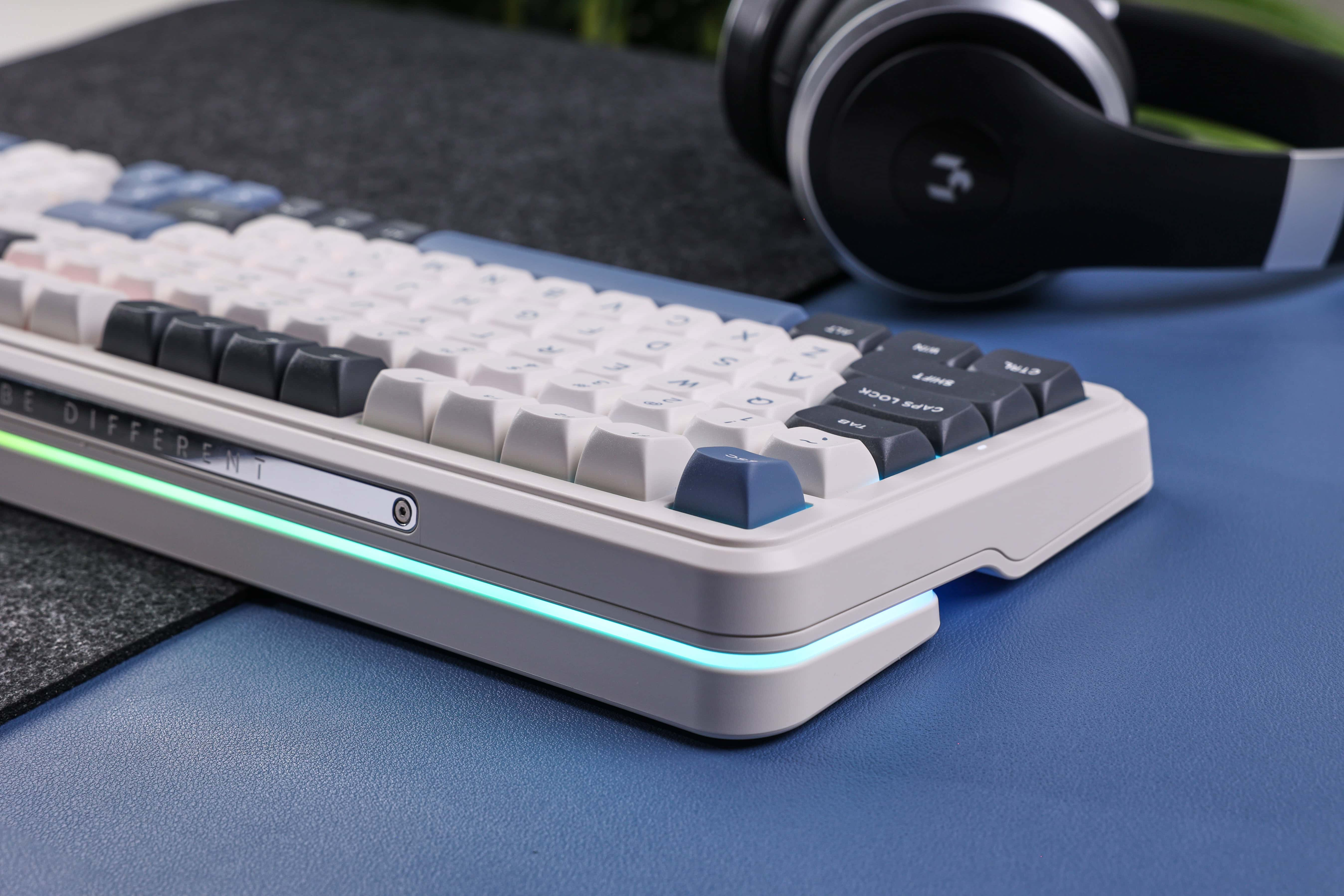 Eine weiße und blaue Tastatur liegt auf einer blauen Oberfläche, im Hintergrund Kopfhörer.