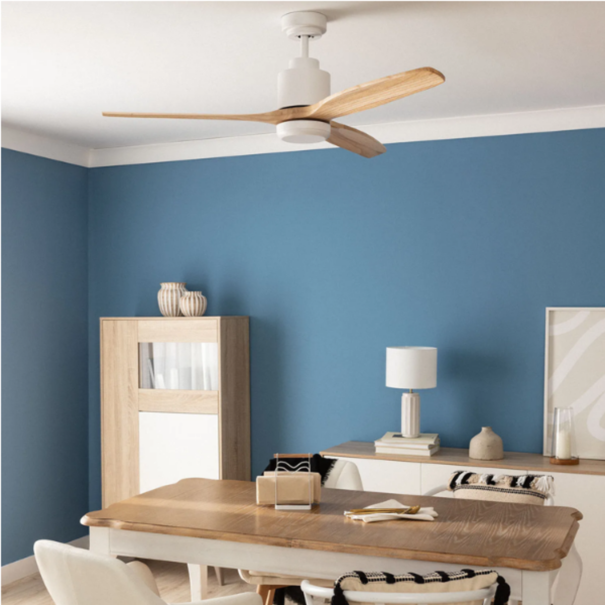 Un ventilatore da soffitto bianco con pale in legno, in una stanza con pareti blu e mobili.