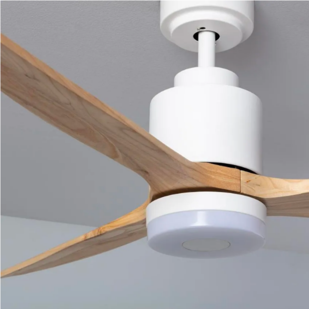 Primo piano di un ventilatore da soffitto bianco con pale in legno e una luce. Il soffitto è bianco.