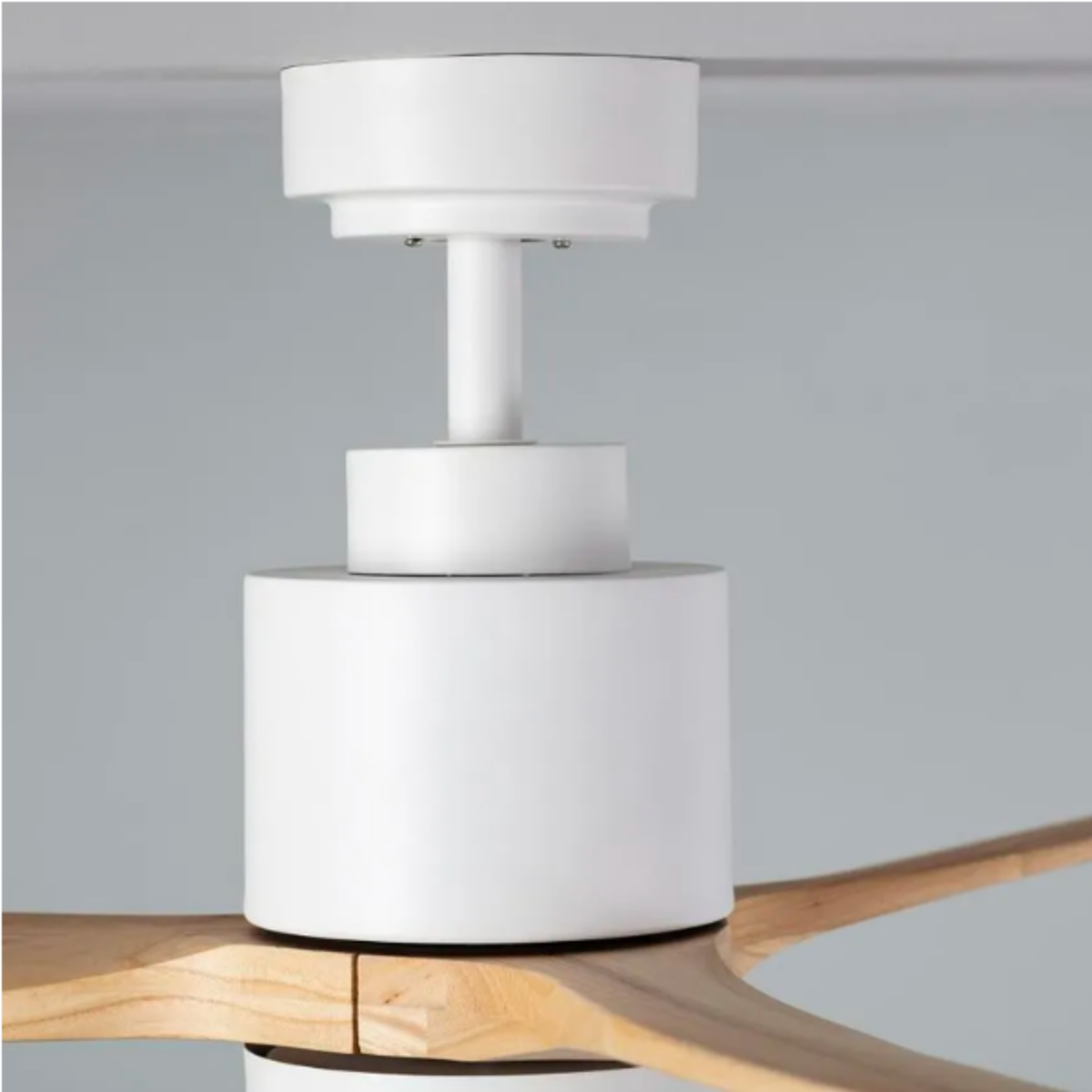 Primo piano dell'alloggiamento del motore di un ventilatore da soffitto bianco e l'inizio delle pale in legno.