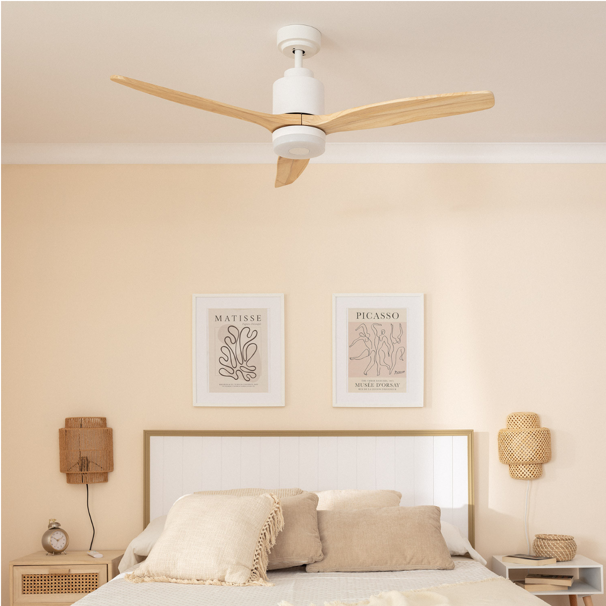 Ventilatore da soffitto bianco con pale in legno in una camera da letto con opere d'arte.