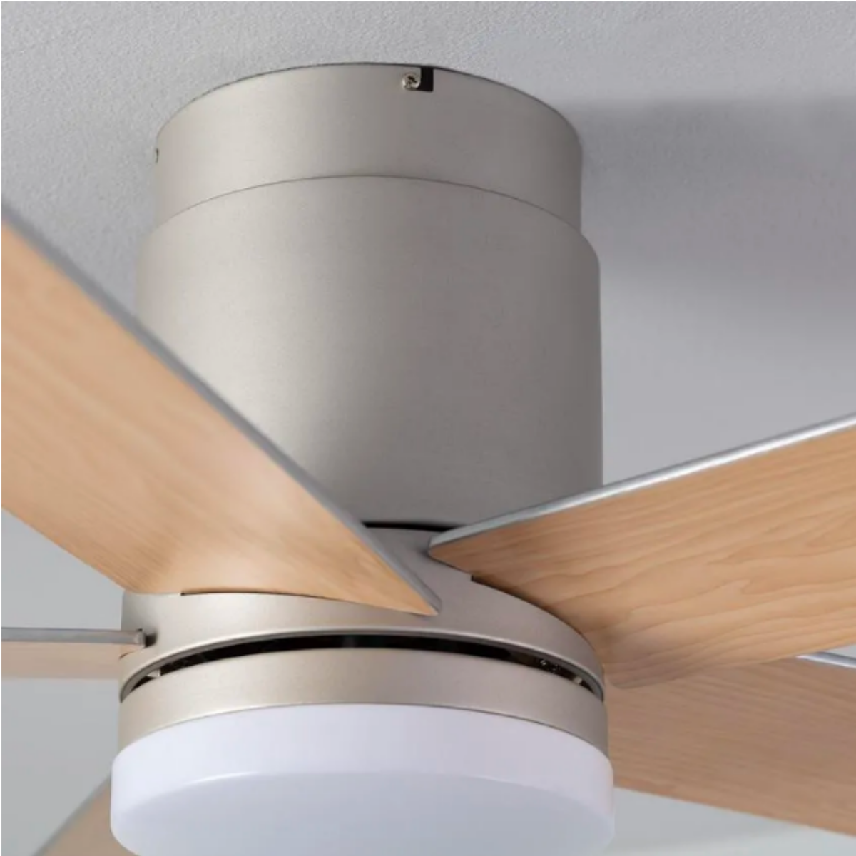 Primo piano di un ventilatore da soffitto con pale in legno chiaro e alloggiamento motore argentato.