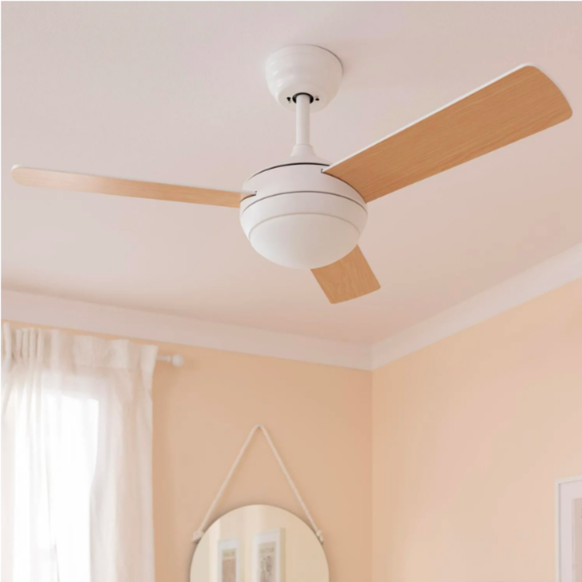 Un ventilatore da soffitto bianco con pale in legno, appeso in una stanza con pareti color pesca.