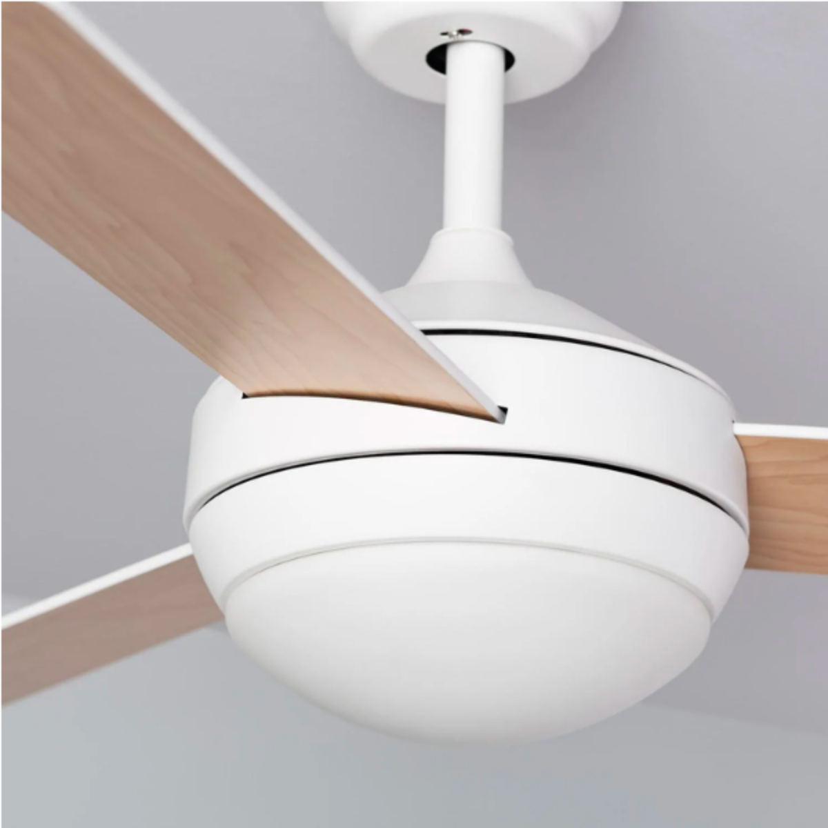 Primo piano di un ventilatore da soffitto bianco con pale in legno, lampada bianca.