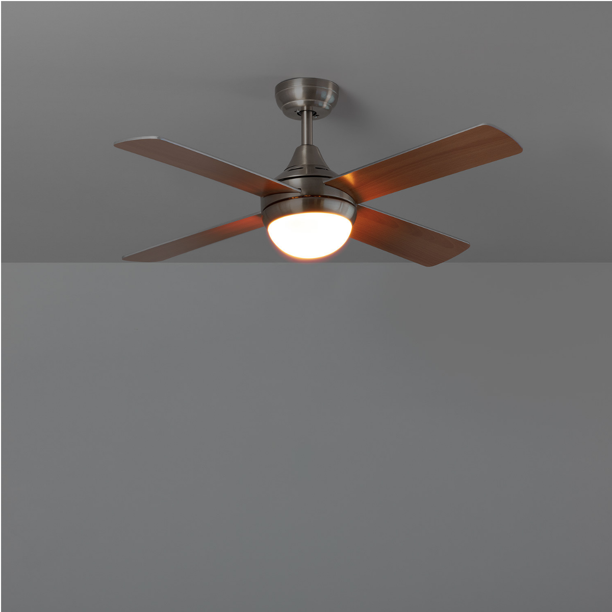 Ventilatore da soffitto con quattro pale in legno e un'illuminazione. La luce è accesa e illumina la stanza.