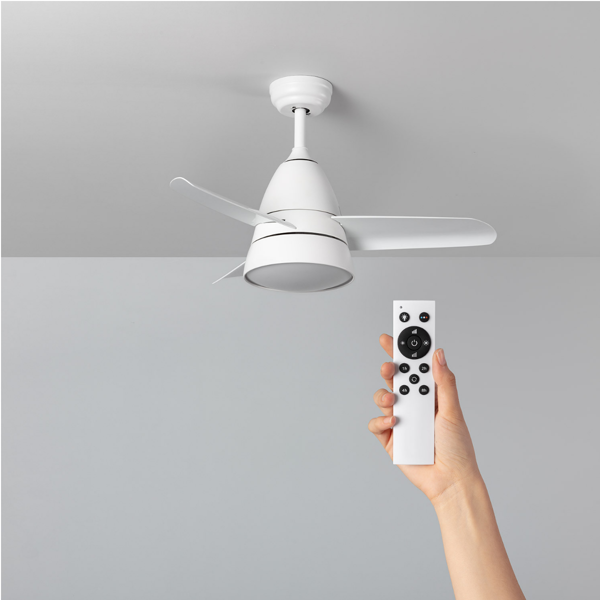 Una mano tiene un telecomando che punta verso un ventilatore da soffitto bianco. Il ventilatore ha pale bianche e un'illuminazione.