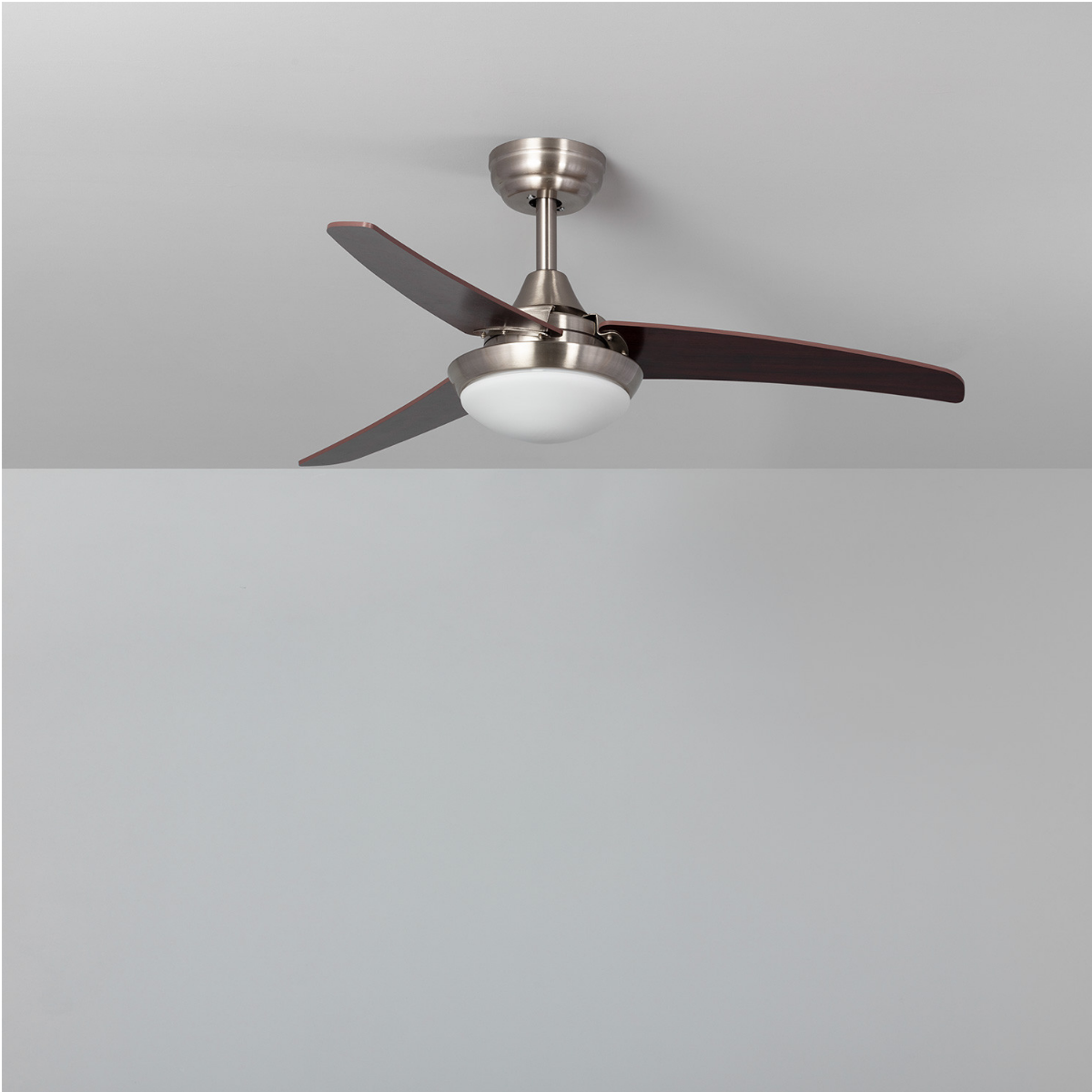 Ventilatore da soffitto, finitura argento, pale in legno scuro, luce bianca, sfondo grigio.