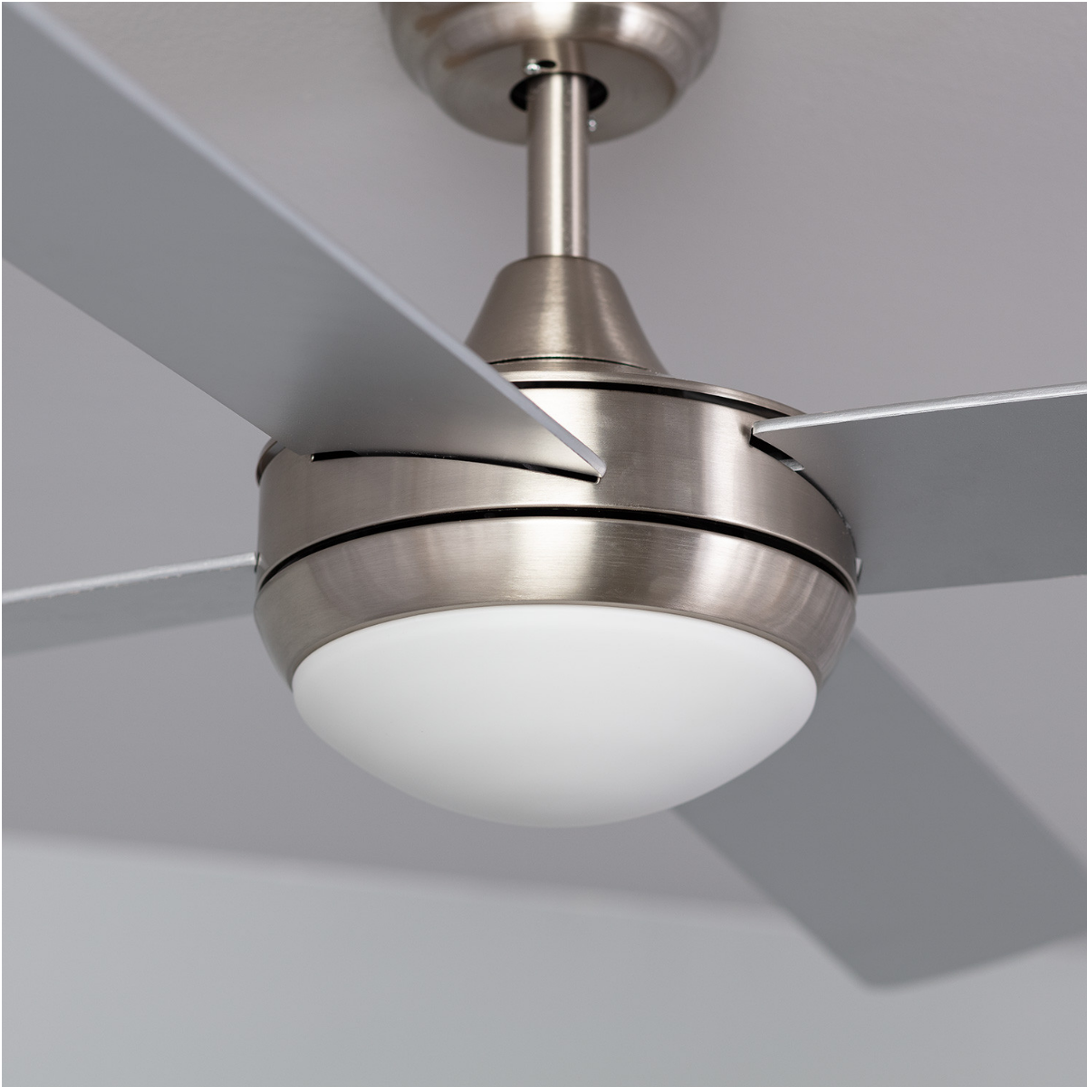 Primo piano di un ventilatore da soffitto argentato. Luce bianca. Sfondo grigio.