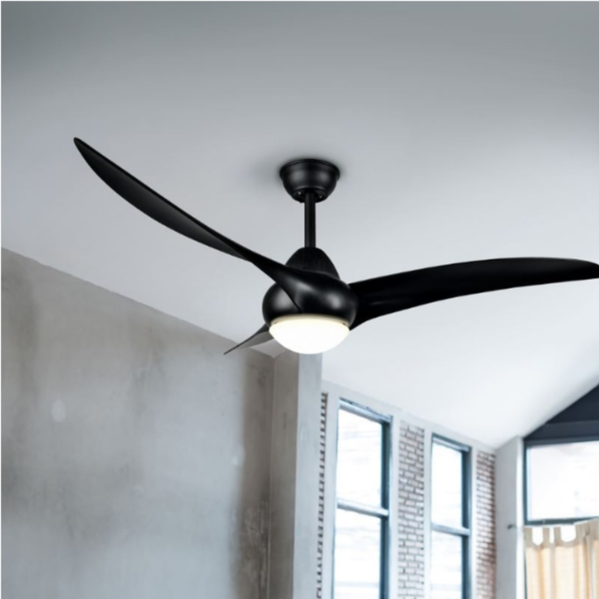 Un ventilatore da soffitto nero con tre pale curve e un'illuminazione centrale è appeso al soffitto. Muro grigio sullo sfondo.