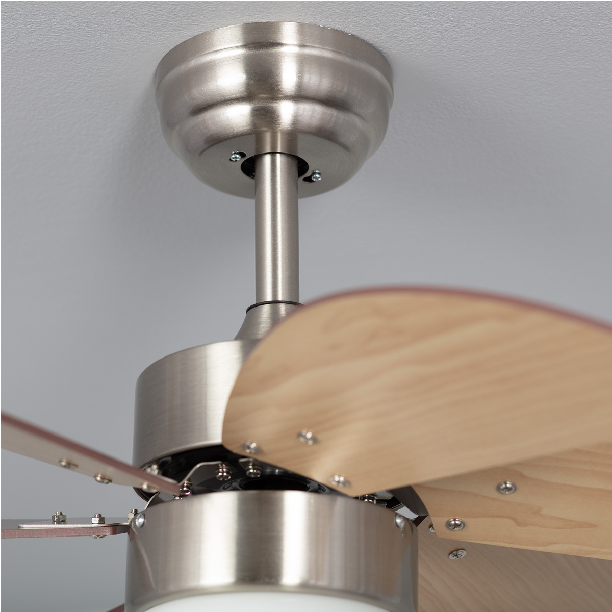 Primo piano del meccanismo del ventilatore da soffitto. Pale in legno chiaro e alloggiamento metallico argentato.