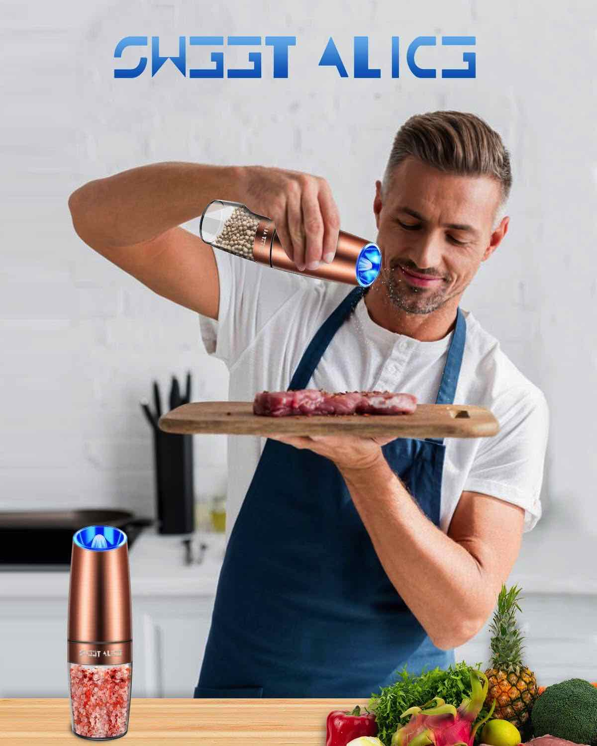 Mann benutzt roségoldenen elektrischen Pfeffermühle auf Fleisch. Andere Mühle, Küche im Hintergrund.