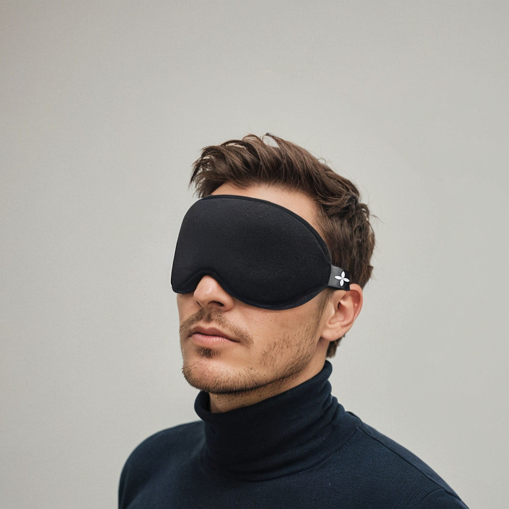 Mann mit schwarzer Augenmaske, vor grauem Hintergrund, nach rechts blickend.