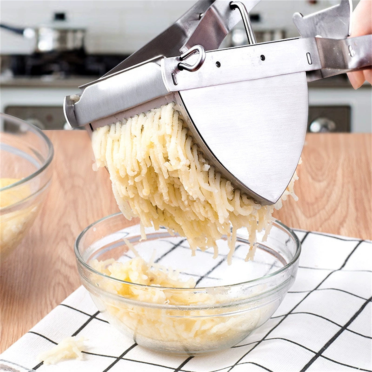 Kartoffelpresse mit gekochten Kartoffeln, die in eine Glasschüssel gepresst werden.